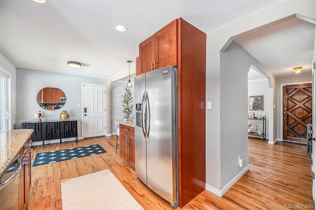 kitchen featuring light stone counters, pendant lighting, light wood-style floors, stainless steel fridge, and baseboards