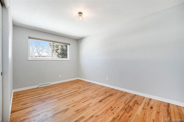 spare room with light wood finished floors, visible vents, and baseboards