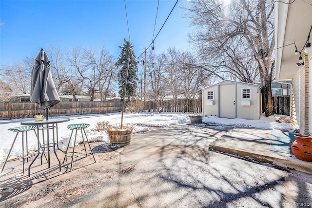 yard layered in snow featuring a storage shed, a fenced backyard, and an outdoor structure