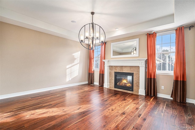 unfurnished living room with a tray ceiling, a tiled fireplace, dark wood-type flooring, and an inviting chandelier