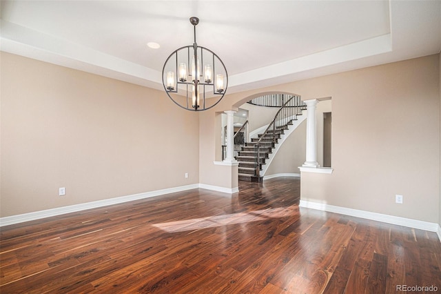 spare room featuring dark hardwood / wood-style floors, a raised ceiling, ornate columns, and an inviting chandelier