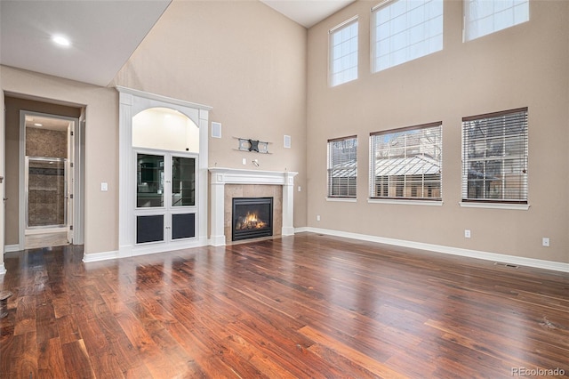 unfurnished living room featuring a tiled fireplace, a wealth of natural light, and dark hardwood / wood-style floors