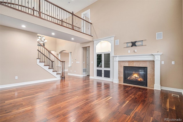 unfurnished living room featuring a high ceiling, hardwood / wood-style flooring, ornate columns, and a tiled fireplace