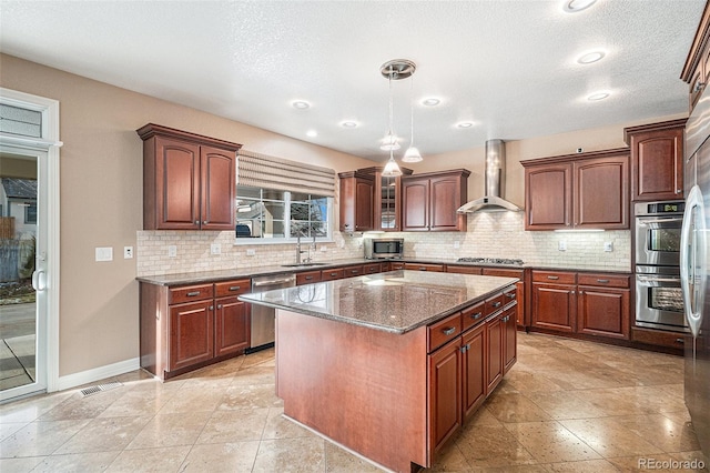 kitchen featuring a center island, sink, stainless steel appliances, wall chimney range hood, and pendant lighting