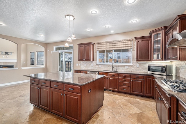 kitchen featuring stainless steel appliances, sink, dark stone countertops, a center island, and hanging light fixtures