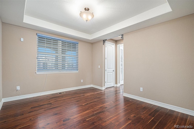 empty room with a tray ceiling and dark hardwood / wood-style flooring