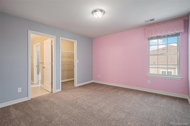 unfurnished bedroom featuring a spacious closet, a closet, light carpet, and a textured ceiling