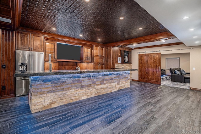 bar with a barn door, dark hardwood / wood-style flooring, dark stone counters, and appliances with stainless steel finishes