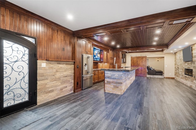 kitchen featuring a center island, dark wood-type flooring, a stone fireplace, wooden walls, and high end fridge