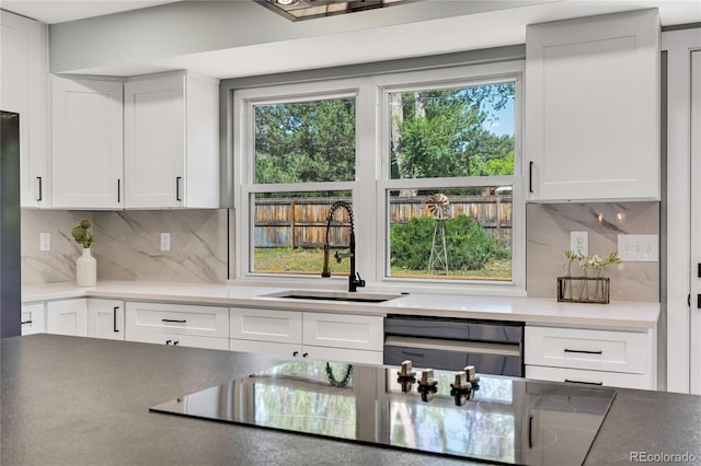 6842 Garland St, Arvada, CO 80004 - kitchen with black electric cooktop, backsplash, white cabinetry, and dishwashing machine