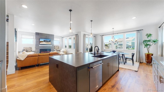 kitchen featuring sink, light hardwood / wood-style flooring, a kitchen island with sink, a fireplace, and stainless steel dishwasher