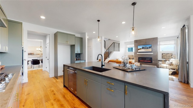 kitchen featuring pendant lighting, sink, a tile fireplace, stainless steel appliances, and a center island with sink