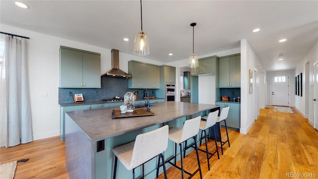 kitchen with tasteful backsplash, wall chimney range hood, light hardwood / wood-style flooring, and stainless steel appliances