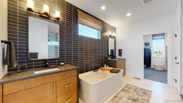 bathroom with tile patterned floors, tasteful backsplash, tile walls, vanity, and a washtub