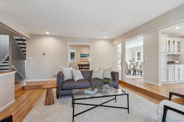 living area with light wood-type flooring, stairs, recessed lighting, and baseboards