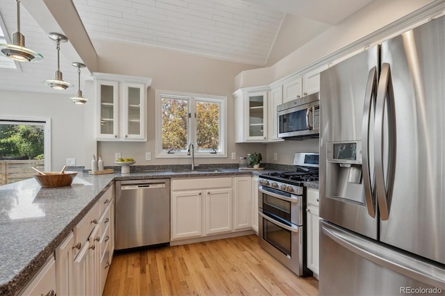 kitchen with stainless steel appliances, a sink, light wood-style flooring, dark stone countertops, and white cabinets