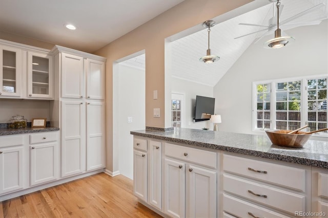 kitchen with light wood-style floors, white cabinets, dark stone countertops, hanging light fixtures, and glass insert cabinets