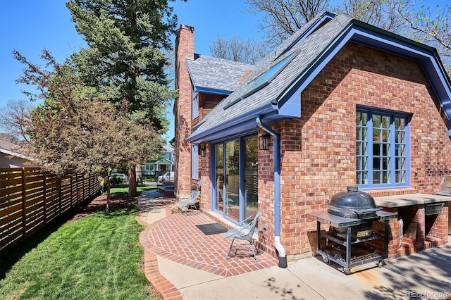 view of side of property featuring brick siding, roof with shingles, a chimney, and a patio area