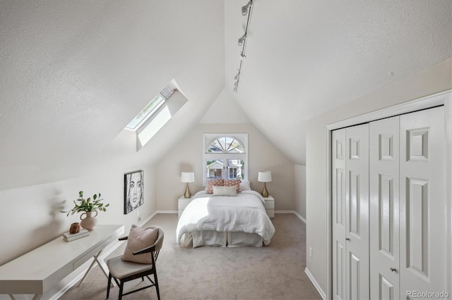 carpeted bedroom featuring rail lighting, vaulted ceiling, a skylight, baseboards, and a closet