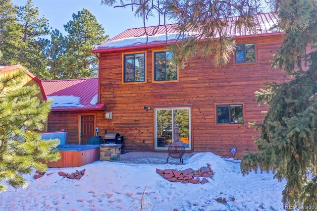 snow covered rear of property with a hot tub and a fire pit