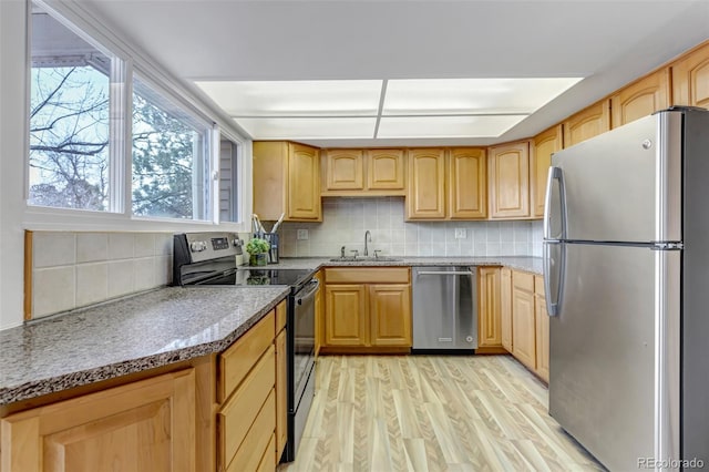 kitchen featuring stainless steel appliances, light brown cabinetry, a sink, and light wood-style flooring