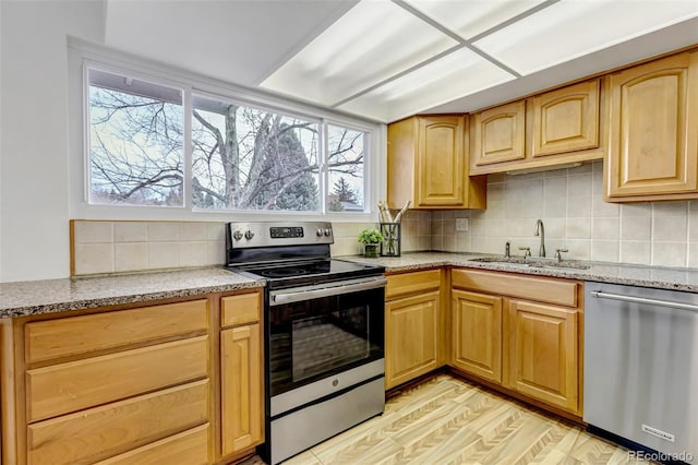 kitchen featuring light stone counters, light wood finished floors, stainless steel appliances, backsplash, and a sink