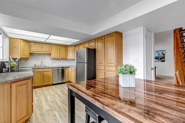 kitchen with light stone counters, a sink, appliances with stainless steel finishes, backsplash, and light wood finished floors