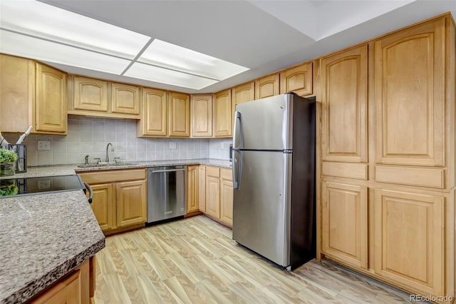 kitchen with stainless steel appliances, light brown cabinetry, a sink, and light wood-style floors