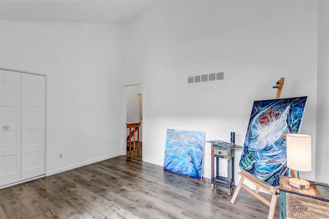 interior space featuring baseboards, visible vents, a high ceiling, and wood finished floors