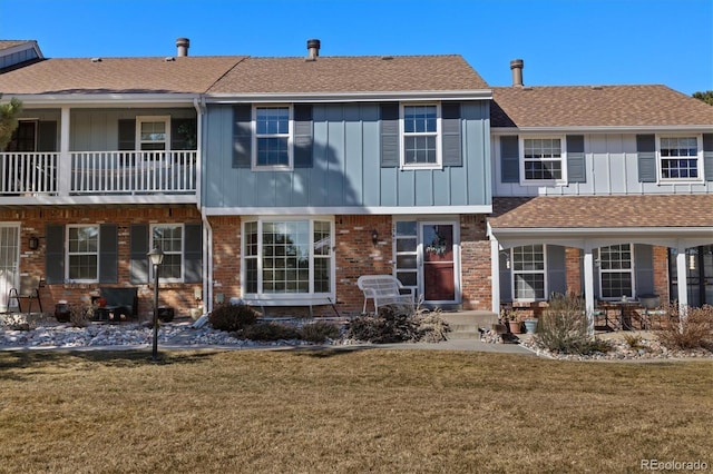 view of front of home featuring board and batten siding, a front yard, brick siding, and roof with shingles