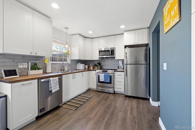 kitchen featuring tasteful backsplash, appliances with stainless steel finishes, dark wood-type flooring, white cabinetry, and a sink