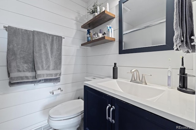 bathroom featuring toilet, wood walls, and vanity