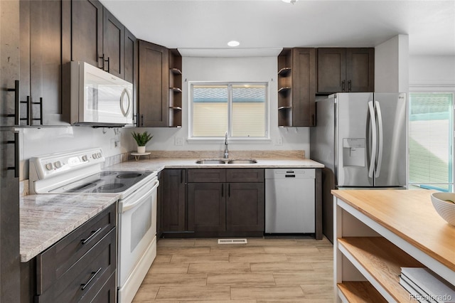 kitchen featuring open shelves, white appliances, dark brown cabinetry, and a sink