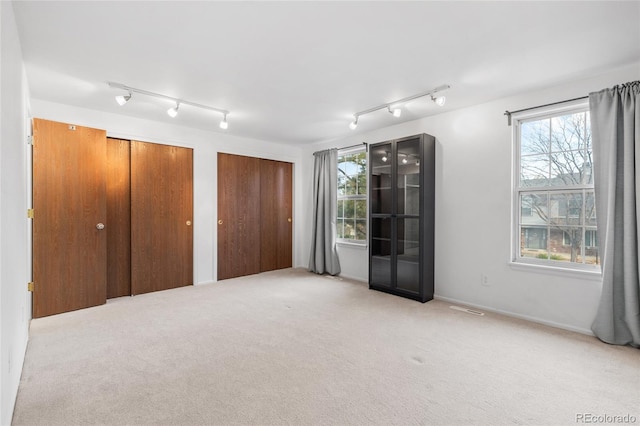 unfurnished bedroom featuring light colored carpet, visible vents, and two closets