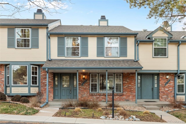 multi unit property with a shingled roof, covered porch, brick siding, and a chimney