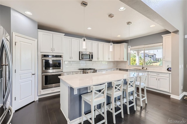 kitchen featuring sink, white cabinetry, decorative light fixtures, a center island, and appliances with stainless steel finishes