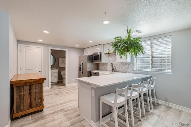 kitchen with a kitchen bar, white cabinetry, appliances with stainless steel finishes, kitchen peninsula, and decorative backsplash