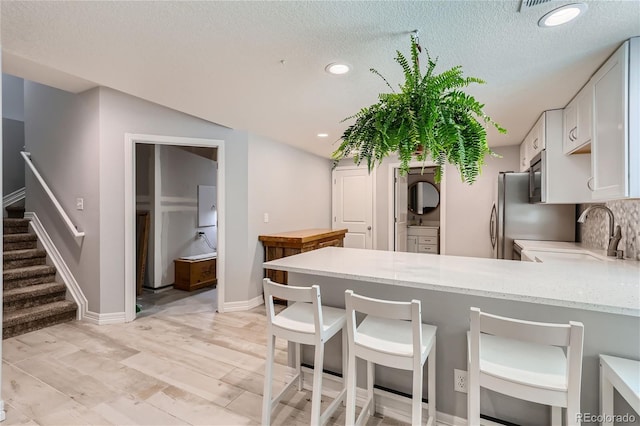 kitchen featuring sink, a textured ceiling, white cabinets, decorative backsplash, and kitchen peninsula