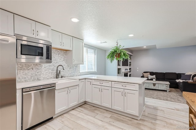 kitchen featuring white cabinetry, sink, backsplash, kitchen peninsula, and stainless steel appliances