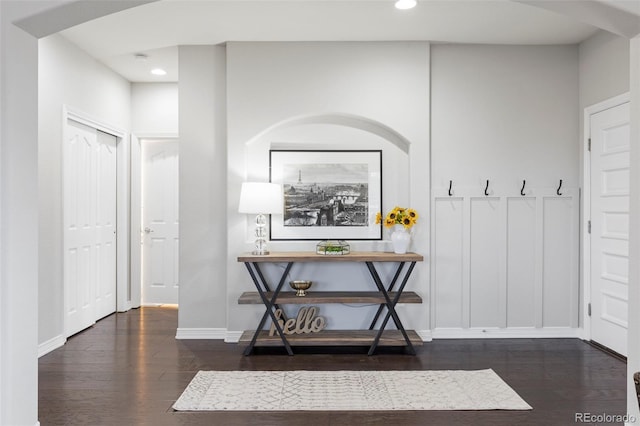 interior space featuring dark wood-type flooring, a decorative wall, recessed lighting, and baseboards