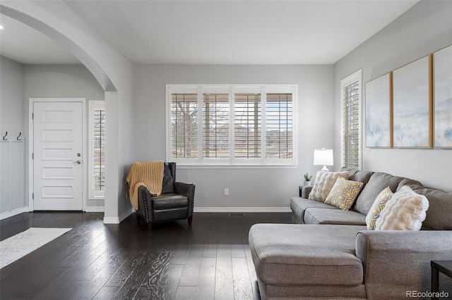 living area featuring dark wood-type flooring, baseboards, and arched walkways