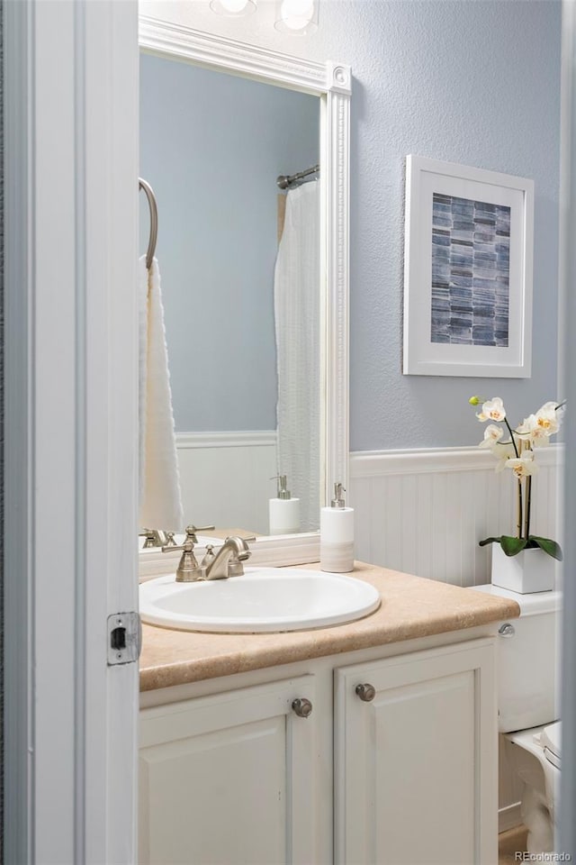 full bathroom with vanity, toilet, and wainscoting