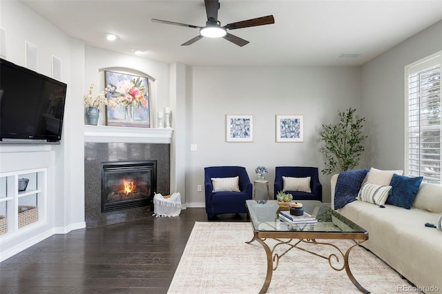 living area with a tiled fireplace, ceiling fan, dark wood-type flooring, and baseboards