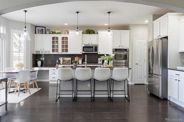 kitchen with backsplash, dark wood finished floors, a breakfast bar area, appliances with stainless steel finishes, and white cabinets