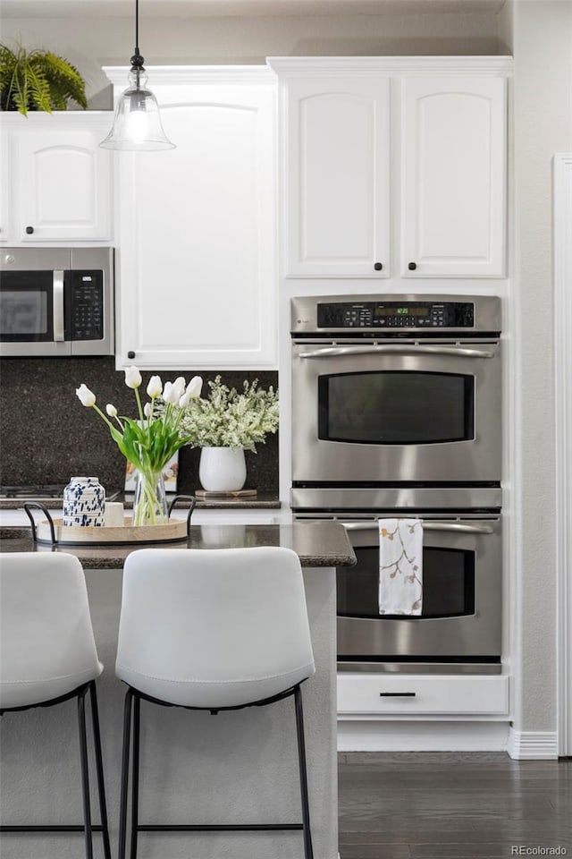 kitchen featuring dark wood-style flooring, white cabinets, appliances with stainless steel finishes, dark countertops, and tasteful backsplash