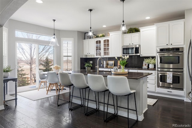 kitchen with dark wood-type flooring, appliances with stainless steel finishes, a kitchen bar, dark countertops, and backsplash