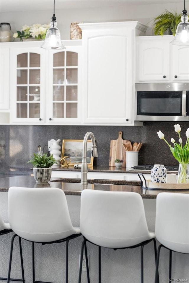 kitchen featuring dark countertops, white cabinets, pendant lighting, stainless steel microwave, and backsplash