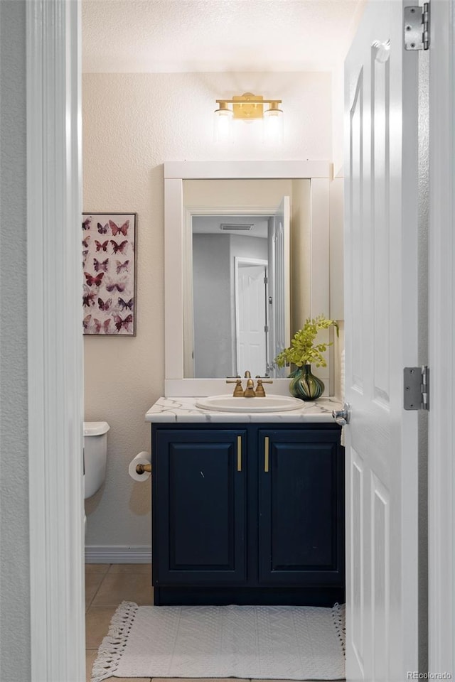 half bath with vanity, tile patterned floors, toilet, and baseboards