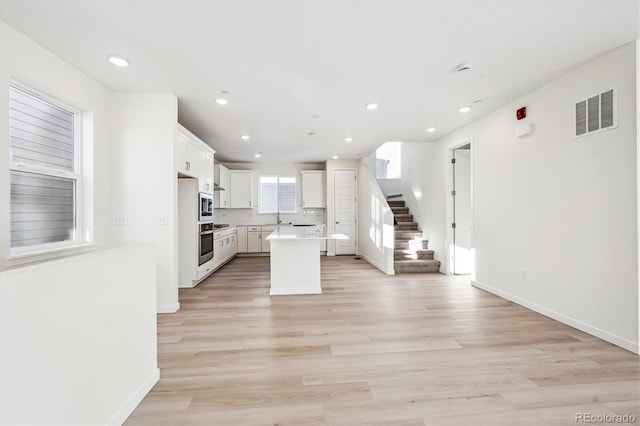 kitchen featuring decorative backsplash, light wood-type flooring, appliances with stainless steel finishes, a kitchen island, and white cabinetry