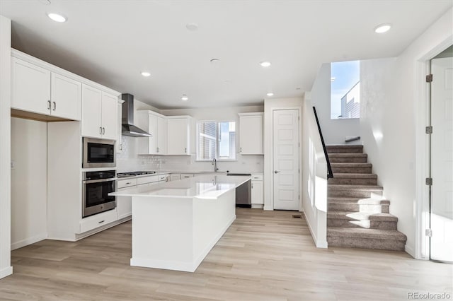 kitchen with a center island, wall chimney range hood, decorative backsplash, appliances with stainless steel finishes, and white cabinetry